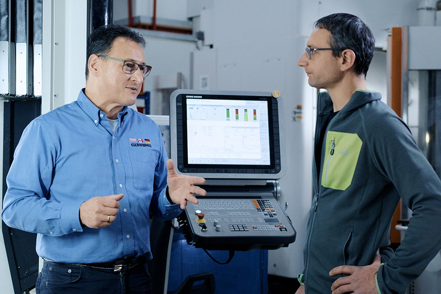 Two men are standing in an industrial setting and discussing something.