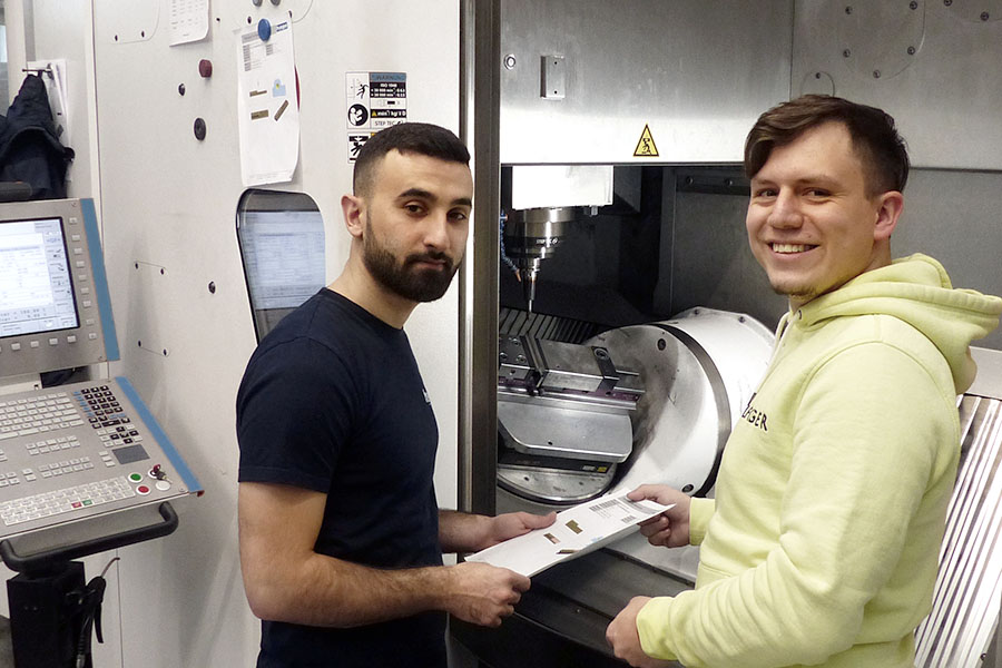 Two technicians check work instructions in front of a CNC machine.