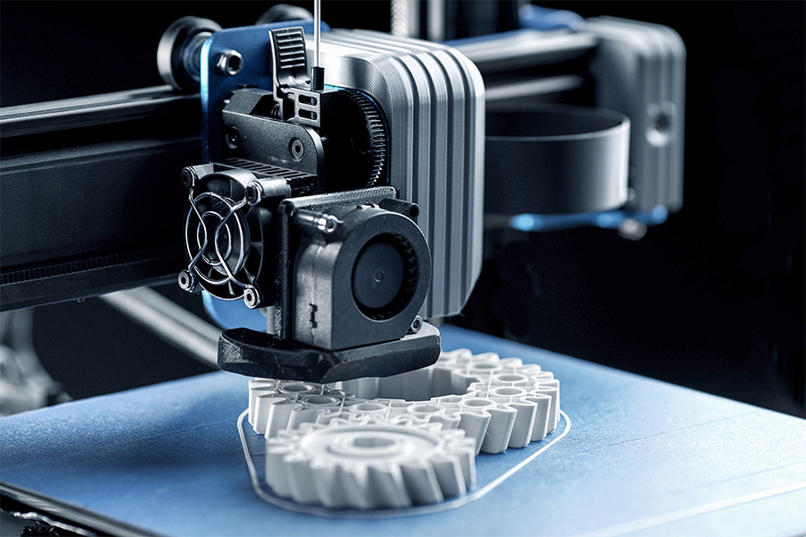 FDM-3D-Drucker, der auf blauem Druckbett ein weißes Zahnrad druckt