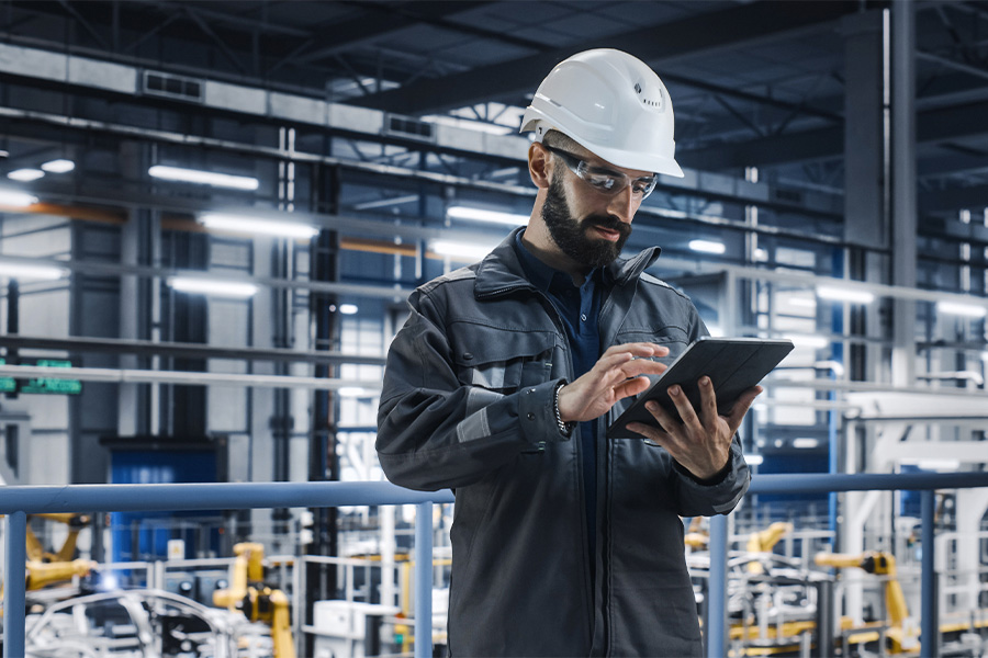 Technician with helmet and safety goggles checks operating data on a tablet in an industrial production hall