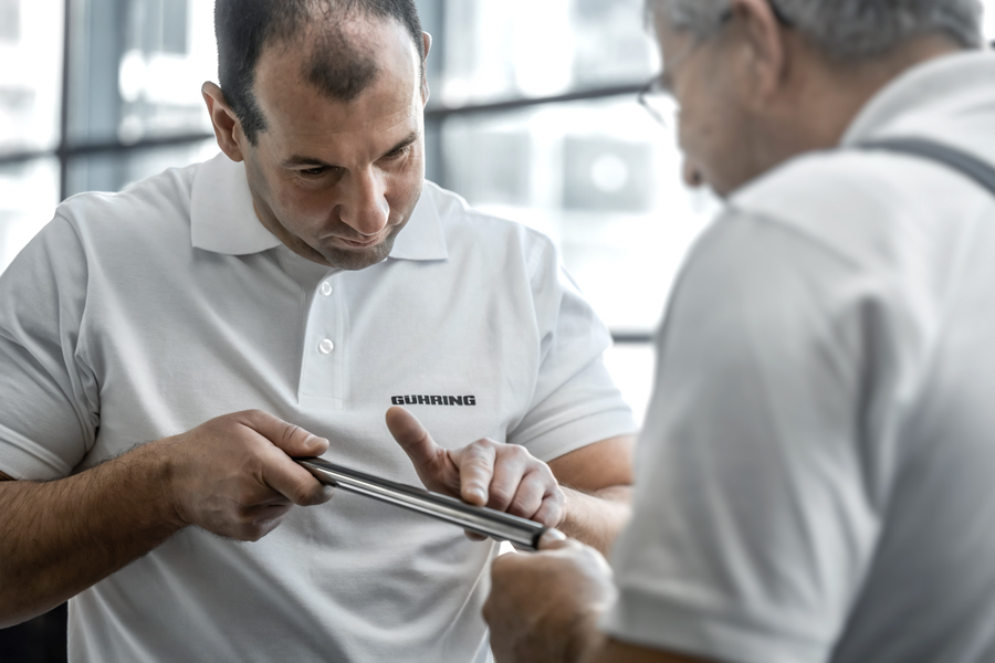 Two specialists in white polo shirts inspect a precision tool together as part of a quality inspection