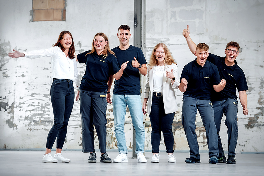 Group of young quality specialists, three men and two women, in an informal setting, all smiling and giving thumbs up