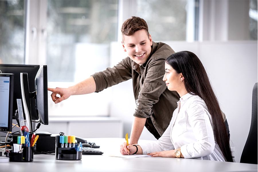 Young man in an office explaining something to a colleague on the computer