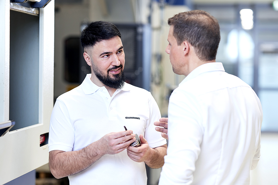 Two employees in an industrial work environment discussing a piece of tooling