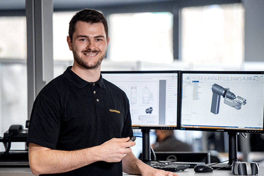 Young employees standing confidently in a modern office with two monitors in the background