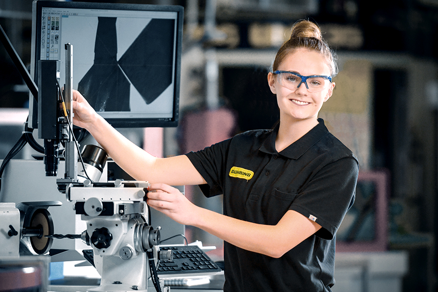 Young female employee wearing safety goggles operates a CNC machine in an industrial setting