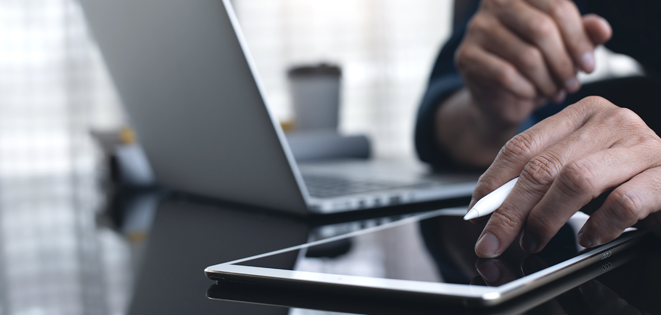 B2B-Kunde nutzt einen Tablet-Stift auf einem digitalen Gerät vor einem Laptop