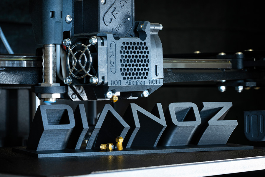 Ein 3D-Drucker erstellt ein großes, dreidimensionales Logo DIANOZ aus einem schwarzen Material