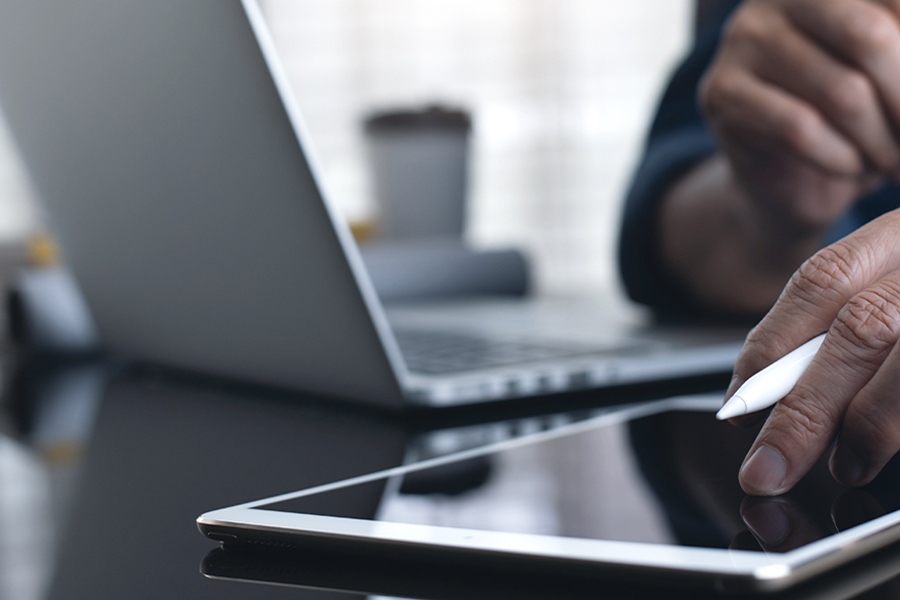B2B-Kunde nutzt einen Tablet-Stift auf einem digitalen Gerät vor einem Laptop B2B-Kunde nutzt einen Tablet-Stift auf einem digitalen Gerät vor einem Laptop