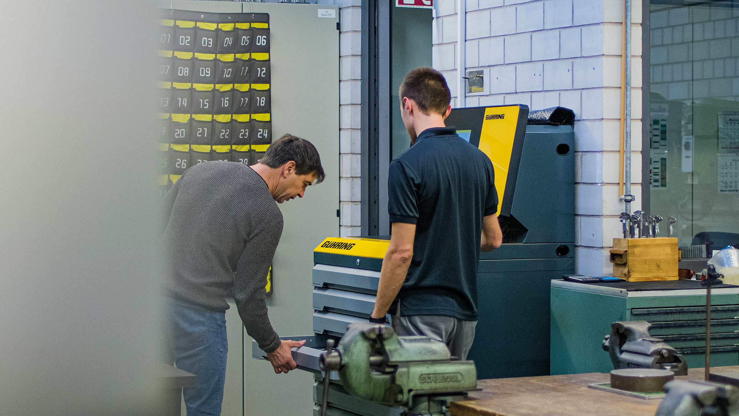Zwei Männer bedienen einen Werkzeugschrank in einer Werkstatt